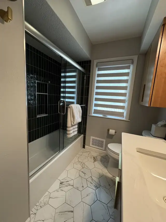 Dark green vertical tile tub shower with a glass door, hexagon floor and window