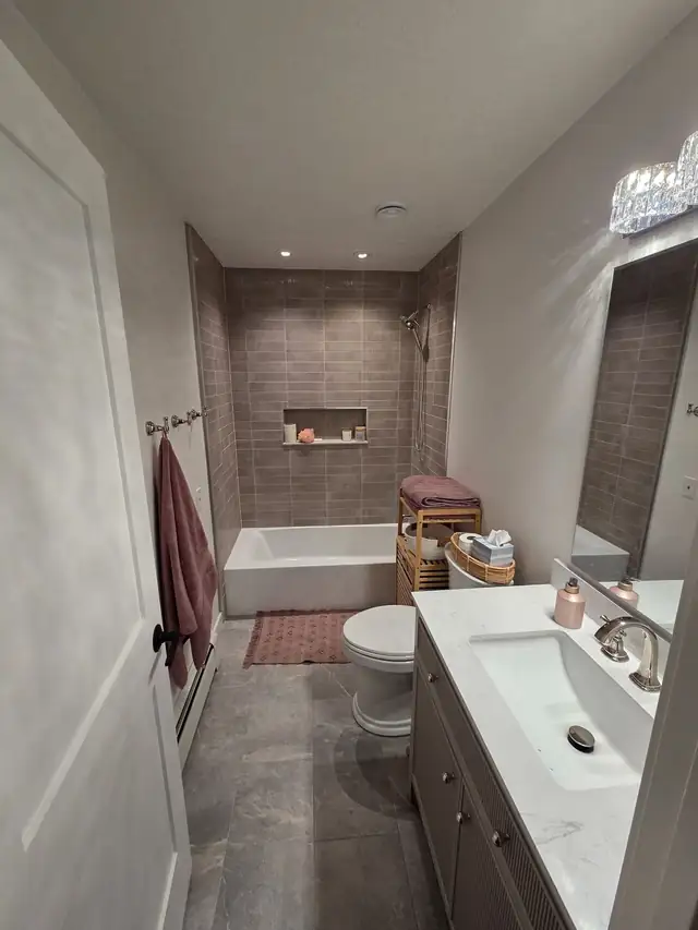Tub alcove in warm mauve tile with a recessed niche and a white vanity