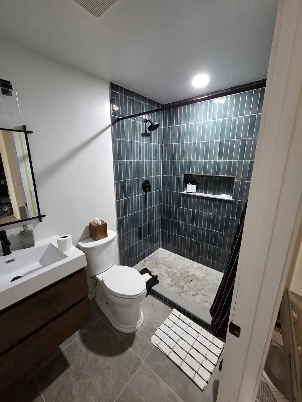 Bathroom remodeling in Minneapolis by CK Tile: walk-in shower in deep blue-green glazed vertical tile with a recessed niche, light hexagon mosaic floor and matte black fixtures
